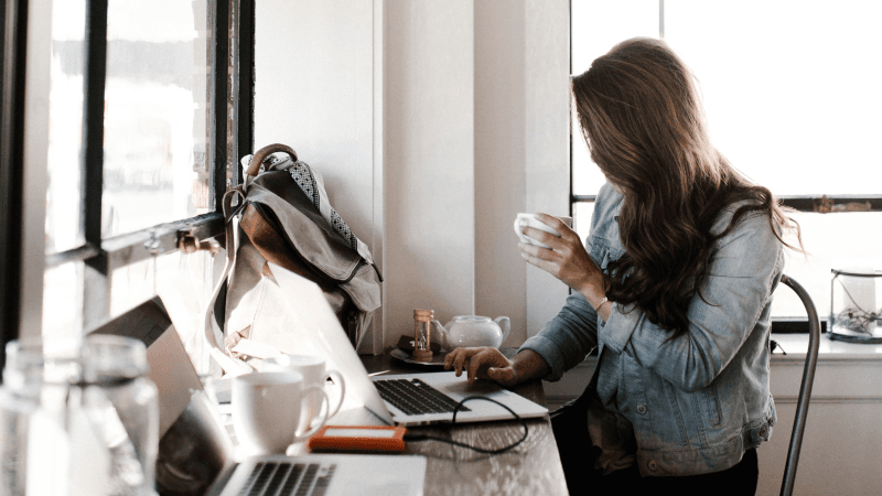 Een vrouwelijke freelance copywriter met haar laptop op het bureau en een kop koffie