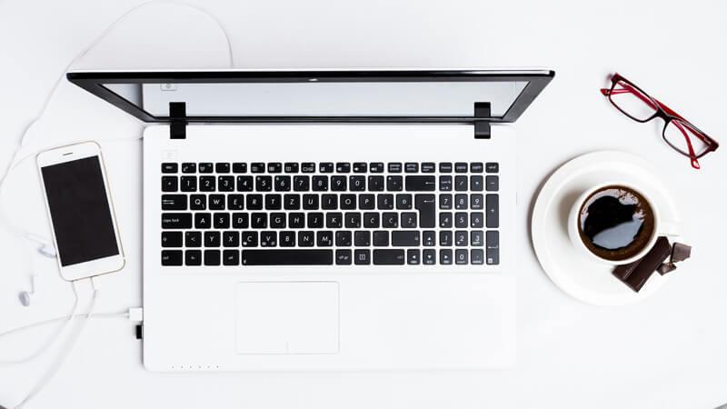 Bureau van een freelance ontwikkelaar met laptop, telefoon en koffie.